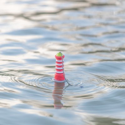Zoom bild av hundleksak flytande fyr gummi tpr vattenleksak hund rep kasta apport röd grå vit grön synlig står upp i vattnet trixie